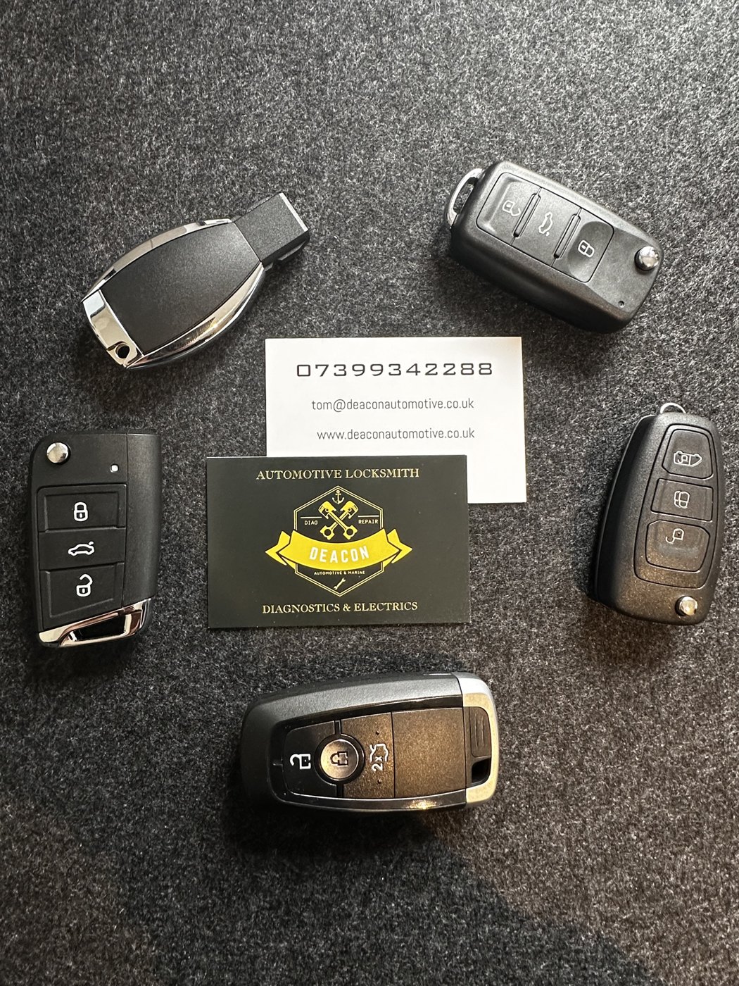 A selection of car key fobs alongside Deacon Automotive business cards